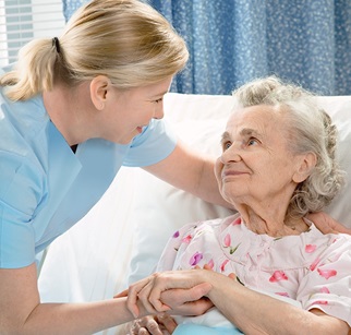 Pflegerin hält Hand und Kopf einer Seniorin im Bett