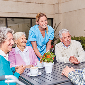 lachende Seniorengruppe am Tisch mit Pflegerin