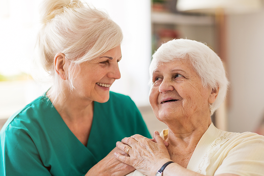 Pflegerin legt lächelnd Hand auf die Schulter einer Seniorin