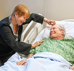 Frau beugt sich über im Pflegebett liegende Seniorin