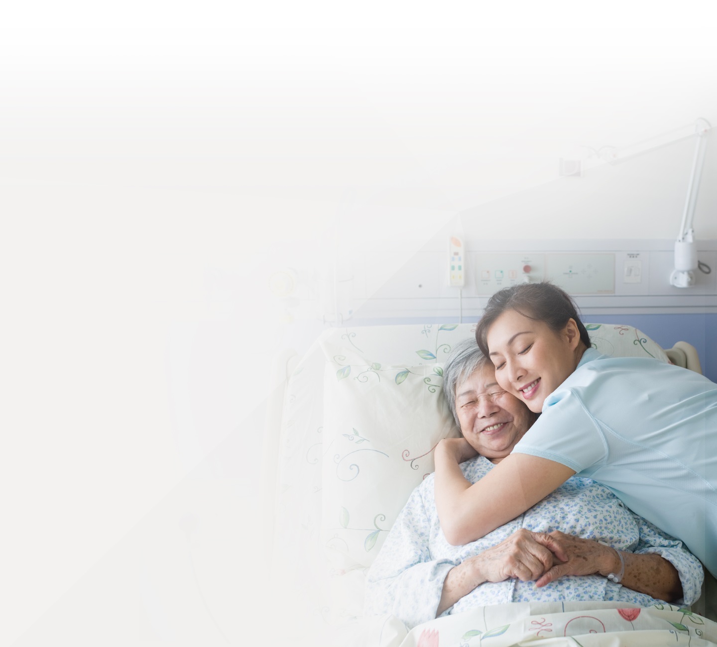 nurse hugging an elderly lady in her hospital bed
